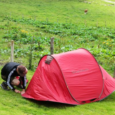 Lukas baut sein Wurfzelt auf der Wiese vor BaumoosAlm​ auf.